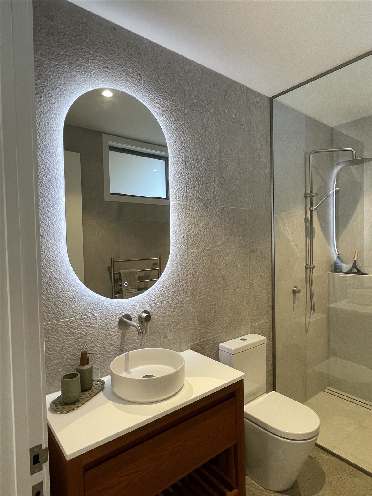 Renovated bathroom with backlit mirror, stone tile, and walk-in shower